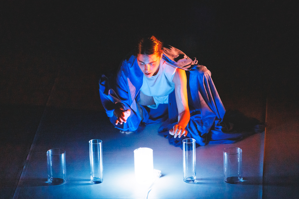 La danseuse Lea Anderson est en position de rituel davant la lumière bleue, création lumière de Jérôme Baudouin, créateur lumière en danse, théâtre et spectacle vivant